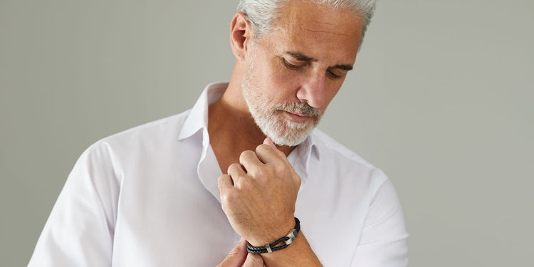 Eleganter Mann mit grauem Haar und Bart in weißem Hemd trägt schwarzes Lederarmband