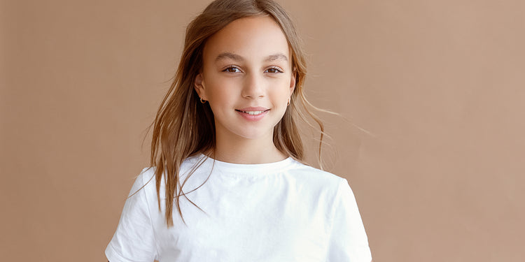 Lächelndes Mädchen mit langen braunen Haaren in weißem T-Shirt trägt kleine goldene Ohrstecker